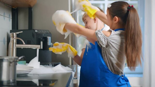 Happy Boy And Girl Kids Washing Dishes And Playing With Foam In Kitchen