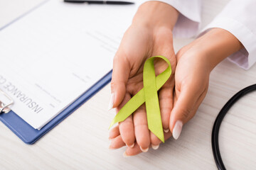 top view of doctor holding green awareness ribbon near insurance claim form, mental health concept