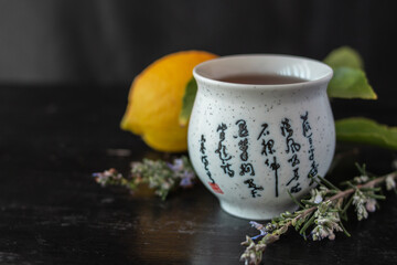 Close-Up shot of asian tea cup with rosemary flowers and lemon in the background.