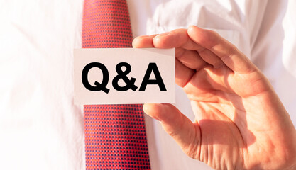 Q and A - Questions and Answers text on paper card in hand of businessman in white shirt and red tie