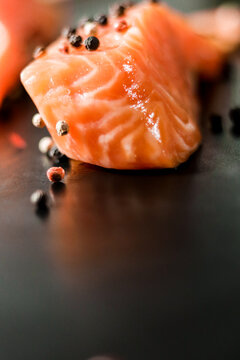 Raw sea red salmon fish fillet uncooked piece with colorful peppercorns on black background.