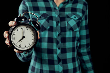 Woman in green shirt holding vintage alarm clock. Black alarm clock in a woman's hand on the black...