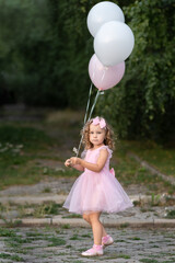 Little girl in pink dress with balloons on the street