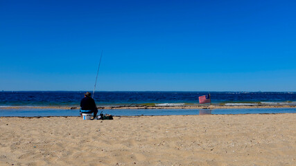 Fisherman Sitting on a Bucket On a Beach with American Flag Nearby (with Copy Space)