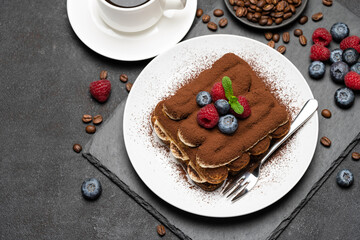 portion of Classic tiramisu dessert with raspberries and blueberries and cup of coffee dark concrete background