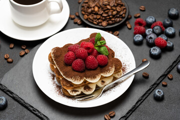 portion of Classic tiramisu dessert with raspberries and blueberries and cup of coffee dark concrete background