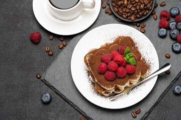 portion of Classic tiramisu dessert with raspberries and blueberries and cup of coffee dark concrete background