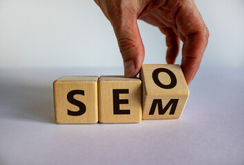 Male hand turns a cube and changes the expression 'SEO' to 'SEM' vice versa. Concept for SEO and SEM or Search Engine Optimization and Search Engine Matketing. Beautiful white background, copy space.