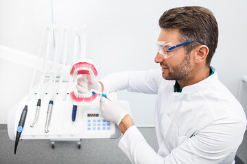 Experienced dentist showing right way brushing teeth in his dental office. Correct teeth cleaning...