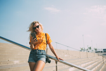 Caucasian hipster girl with retro camera standing at urbanity using cellphone for online banking...