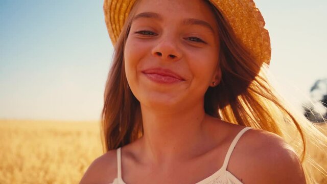 joyful girl in white dress and straw hat walking in wheat field