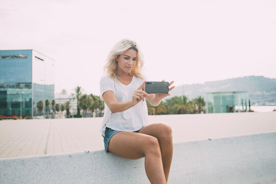 Millennial hipster girl with blonde hairstyle using cellphone camera for shooting video online translation during travel journey, Caucasian blogger connecting to 4g for making content pictures