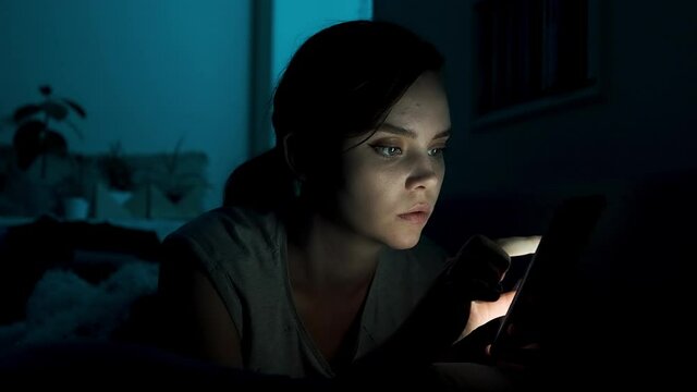Girl read phone at night. Young woman scrolling smartphone and reading news in the bed. Look up social media before sleep