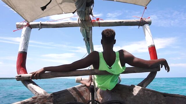 Back of a Young Black African man on a wooden Sail Dhow boat Sit on the Nose and Looking Forward in Green t-shirt Hakuna Matata