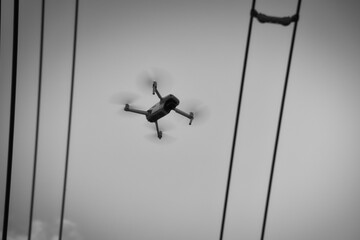 Eine Drohne steht fliegend in der Luft zwischen Stromleitungen