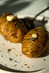 Two baked potatoes with butter, salt and thyme on white plate.