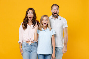 Shocked young parents mom dad with child kid daughter teen girl in basic t-shirts hold index finger up with great new idea isolated on yellow background studio portrait. Family day parenthood concept.