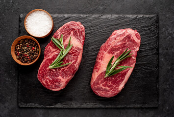Two raw beef ribeye steaks with spices on stone background