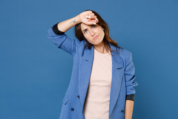 Exhausted tired displeased dissatisfied young brunette woman 20s in basic jacket standing put hand on head having headache looking camera isolated on bright blue colour background studio portrait.