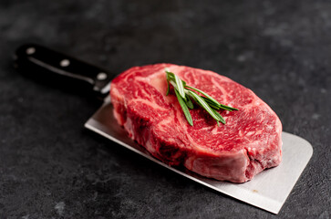 Raw marbled beef steak on a meat knife on a stone background