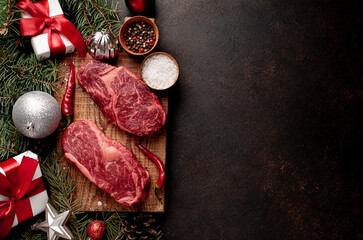 Raw ribeye beef steaks for preparing a dinner for two for a Christmas holiday on a stone table with a Christmas tree and Christmas tree decorations with copy space	