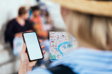 Female traveler with city map and smartphone choosing route for walking