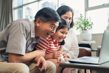 Asian little kids girl having enjoyment together with her grandparents and laptop in the living room atmosphere.