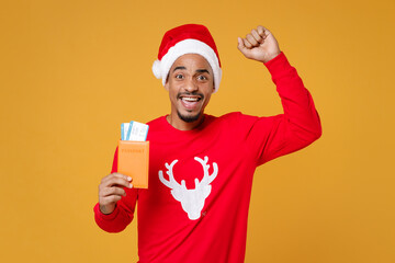 Happy young african american traveler tourist Santa man in Christmas hat hold passport tickets doing winner gesture isolated on yellow background. Happy New Year celebration merry holiday concept.