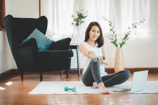 Healthy Beautiful Asian Woman Sitting On The Floor Holding Dumbbell With Laptop At Home In Living Room