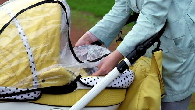 mom covers the stroller with a transparent raincoat from the rain, baby carriage rain raincoat