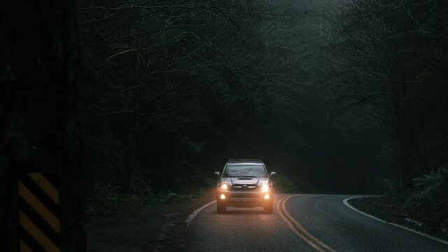 Following car shot through a moody forest with headlights on. Shot of a Toyota 4runner.