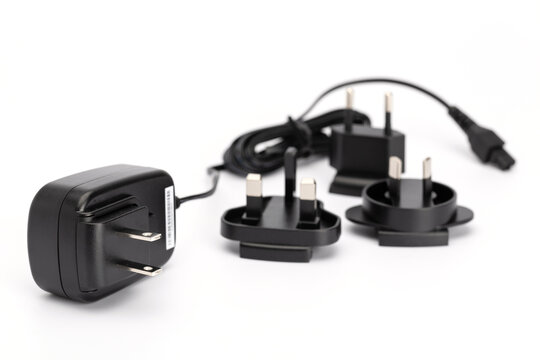 Black plug-in power supply with plug for USA with interchangeable plugs for Europe, Australia and Great Britain in the background