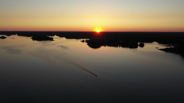 Aerial view of a motorboat, driving in middle of islands, serene, summer sunset, in the Swedish archipelago, Baltic sea, in Sweden - Reverse, drone shot