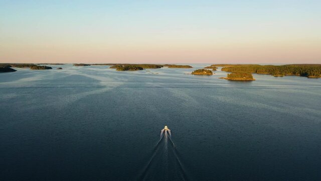 Aerial view of a boat, driving in middle of islands, colorful, summer sunset, in the Swedish archipelago, at the Gulf of Bothnia, in Sweden - Dolly, drone shot
