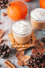 Pumpkin latte on worn wooden table with cedar cones and dry leaves. Autumn still life with pumpkin smoothie decorated with whipped cream closeup