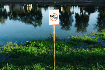 No swimming sign. Entering water is forbidden. Safety lake shore restrictions. Shallow water danger background. Small forest fishing pond.