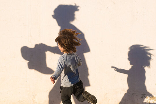 A boy plays running with his and his mother's shadow cast on a nearby wall.