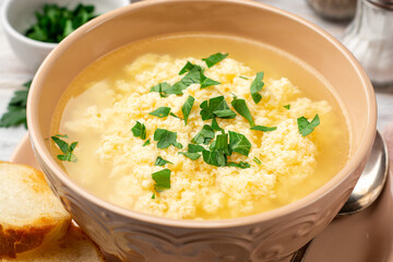Italian stracciatella egg drop soup with parmesan cheese and parsley in bowl on rustic wooden background