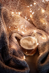 cup of ceoffee stays on a knitted blanket in a golden New Year's garland. Image in black key with noise effect