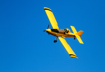 Yellow crop duster banking in a right hand turn against a blue sky
