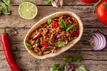 Mexican barquita taco with beef, chilli, tomato, onion and spices on wooden table	