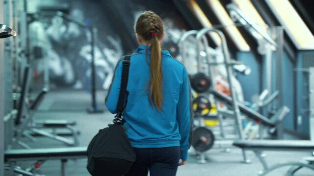 Young woman in sportswear entering gym and putting bag on bench. Following shot athletic female before training indoors. Concept of fitness