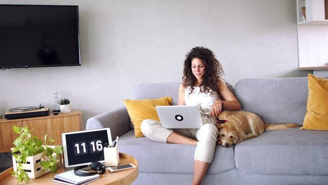 Woman with pet dog sitting indoors at home, using laptop.