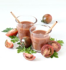 Black tomato juice in a glass with bamboo straws on a light background