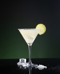 Typical Mexican margarita cocktail with lime slice and ice on black and green background.