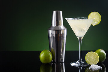 Typical Mexican margarita cocktail with lime slice ice and cocktail shaker on  black and green background. with copy space