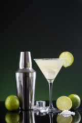 Typical Mexican margarita cocktail with lime slice ice and cocktail shaker on  black and green background.