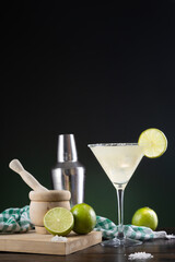 Typical Mexican margarita cocktail with limes and cocktail shaker on  black and green background on wooden base.