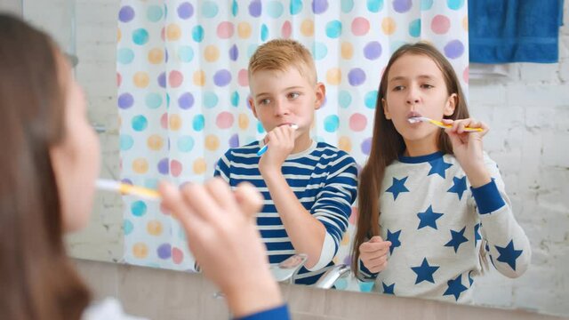 Cute brother and sister kids in pajama brushing teeth looking into bathroom mirror