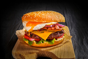 Beef burger with melted cheese and bacon and egg on wooden background